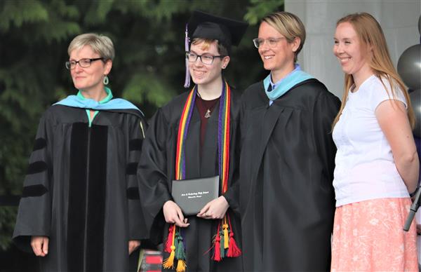 An Arts and Technology High School Graduate receives his diploma and takes a picture with staff.